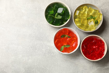 Different jelly cubes in bowls on grey table, flat lay. Space for textの写真素材