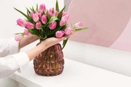 Woman with bouquet of beautiful tulips near window sill indoors, closeup. Space for textの写真素材