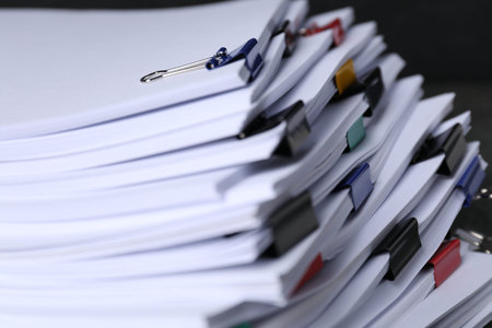Colorful binder clips with sheets of paper on black background, closeup