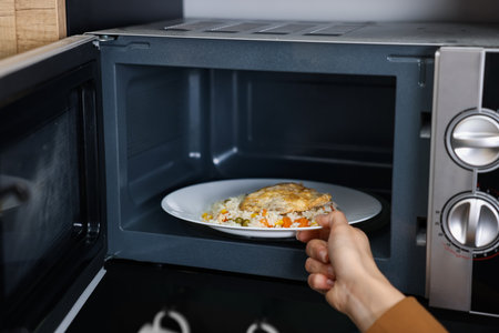 Woman putting plate with lunch into microwave indoors, closeupの写真素材