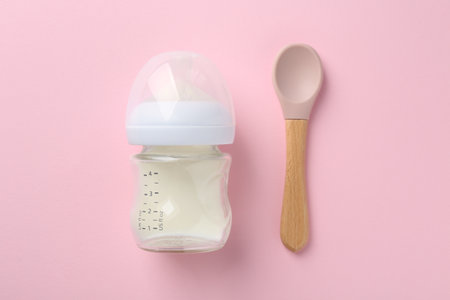 Feeding bottle with milk and spoon on pink background, flat layの写真素材