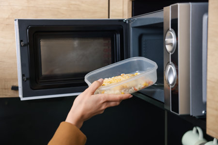 Woman putting container with lunch into microwave indoors, closeupの写真素材