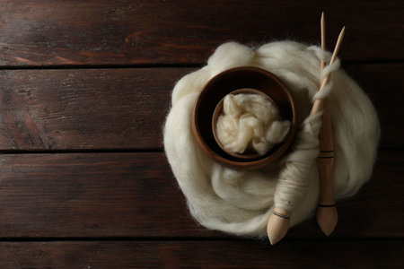 Soft white wool and spindles on wooden table, top view. Space for textの写真素材