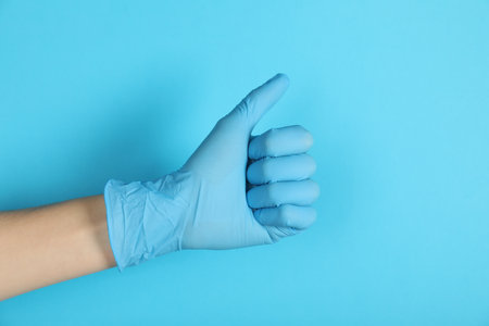 Doctor in medical glove showing thumbs up on light blue background, closeupの写真素材