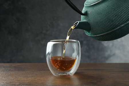 Pouring freshly brewed tea from teapot into cup at wooden table, closeupの写真素材