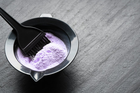 Bowl with hair bleaching powder and brush on black table, closeup. Space for textの写真素材