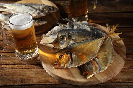 Dried fish and glasses of beer on wooden table, closeup