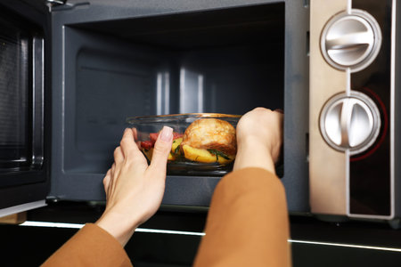 Woman putting container with lunch into microwave indoors, closeup