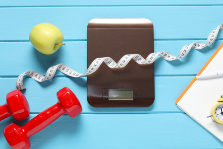 Electronic kitchen scale, measuring tape, dumbbells and apple on light blue wooden table, flat lay. Dietの写真素材