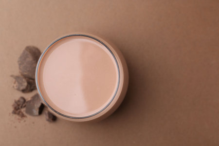 Tasty chocolate milk in glass and pieces of chocolate on brown background, flat lay. Space for textの写真素材