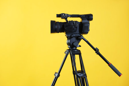 Modern video camera with tripod on yellow background, space for textの写真素材