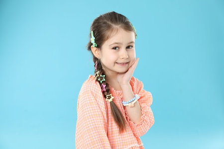 Little girl wearing beautiful hair accessories on light blue background