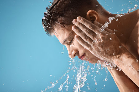 Handsome man washing his face on blue background. Space for textの写真素材