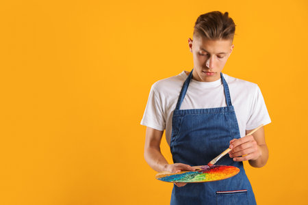 Man with palette and paintbrush on orange background. Space for textの写真素材