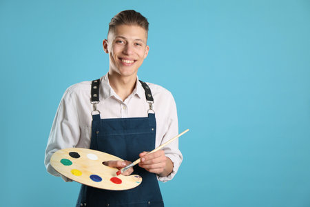 Smiling man with wooden palette and paintbrush on light blue background. Space for textの写真素材