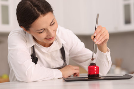 Confectioner decorating delicious dessert with piece of chocolate at tableの写真素材