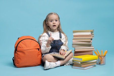 Schoolgirl with backpack and books on light blue backgroundの写真素材