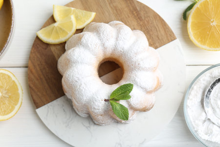 Delicious lemon cake with powdered sugar, mint and citrus fruits on white wooden table, flat lay
