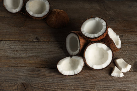 Pieces of cracked coconuts on wooden table, space for textの写真素材