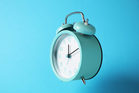 Turquoise alarm clock in air on light blue backgroundの写真素材