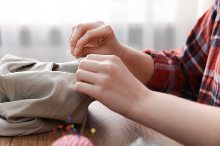 Woman sewing cloth with thread at wooden table indoors, closeupの写真素材