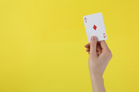 Woman with playing card against yellow background, closeup.の写真素材