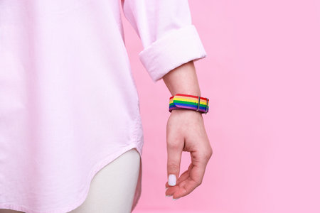 Woman wearing wristband in LGBT colors on pink background, closeup. Space for textの写真素材