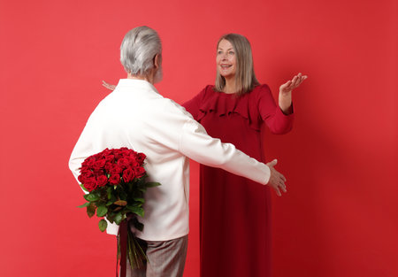 Man hiding bouquet of roses for his happy wife on red background, back viewの写真素材