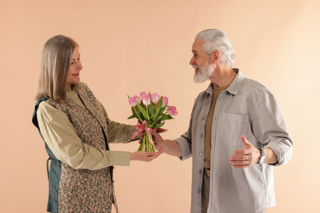 Man presenting bouquet of pink tulips to his wife on beige backgroundの写真素材