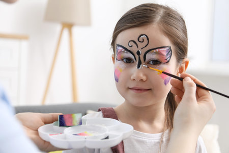 Animator drawing butterfly on girl's face indoors, closeup