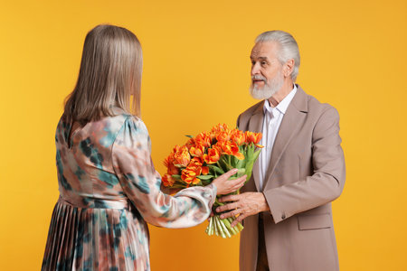 Man presenting bouquet of tulips to his wife on yellow backgroundの写真素材