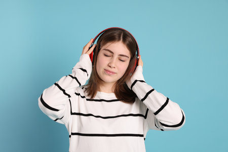 Portrait of teenage girl in headphones listening to music on light blue backgroundの写真素材