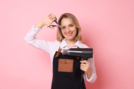 Smiling hairdresser with dryer and scissors on pink backgroundの写真素材