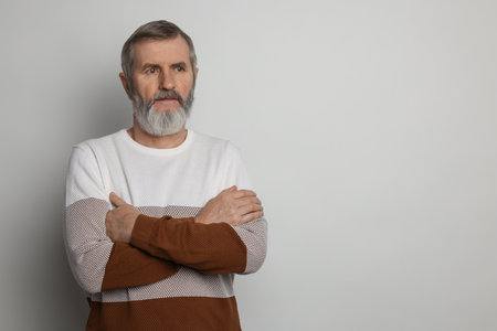 Portrait of mature man with crossed arms on light grey background, space for textの写真素材