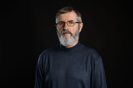 Portrait of mature man in glasses on black background