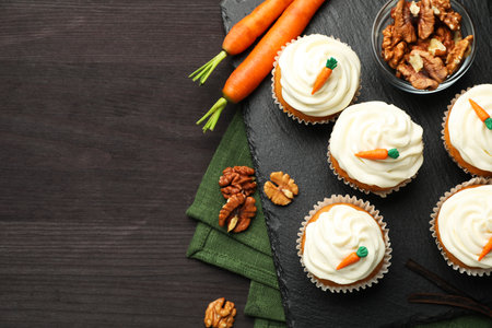 Tasty carrot muffins with cream, walnuts and fresh vegetables on black wooden table, flat lay. Space for textの写真素材