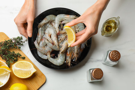 Woman squeezing lemon onto raw shrimps at white marble table, top viewの写真素材
