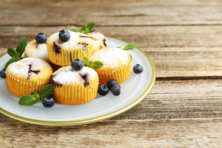 Delicious muffins with blueberries, powdered sugar and mint on wooden table, closeup. Space for textの写真素材
