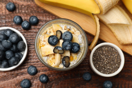 Delicious chia pudding with blueberries, banana and oatmeal in glass on wooden table, flat layの写真素材