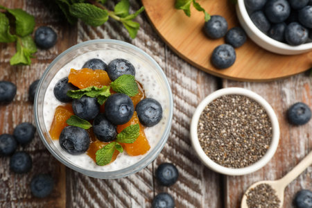 Delicious chia pudding with blueberries, peaches and mint in glass on wooden table, flat layの写真素材