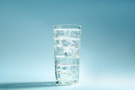 Soda water with ice cubes in glass on light blue background