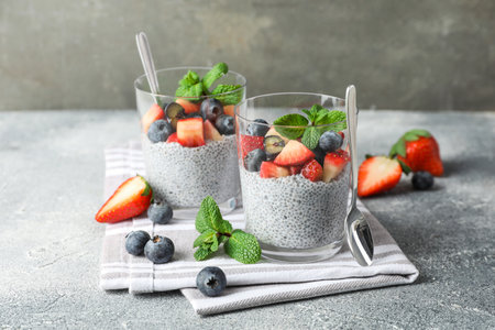 Delicious chia pudding with strawberries, blueberries and mint in glasses on grey tableの写真素材