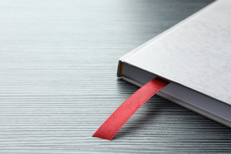 Book with red ribbon bookmark on black wooden table, closeup.