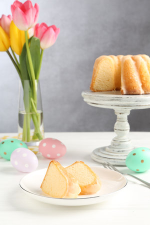 Pieces of delicious bundt cake, Easter eggs and tulips on white wooden table
