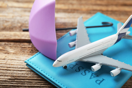 Travel insurance. Plane model, passport and small umbrella on wooden table, closeupの写真素材