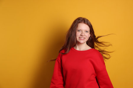 Beautiful teenage girl with freckles on orange background, space for textの写真素材