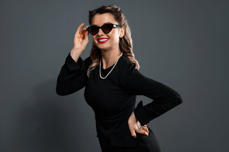 Happy woman in sunglasses on grey background. Pin-up vibe portrait