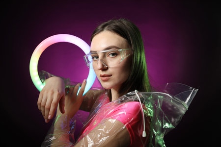Stylish woman wearing transparent coat and glasses on dark purple background