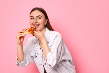 Beautiful woman eating pizza on pink background, space for text