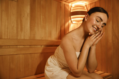 Beautiful woman wrapped in towel on bench at sauna. Space for textの写真素材
